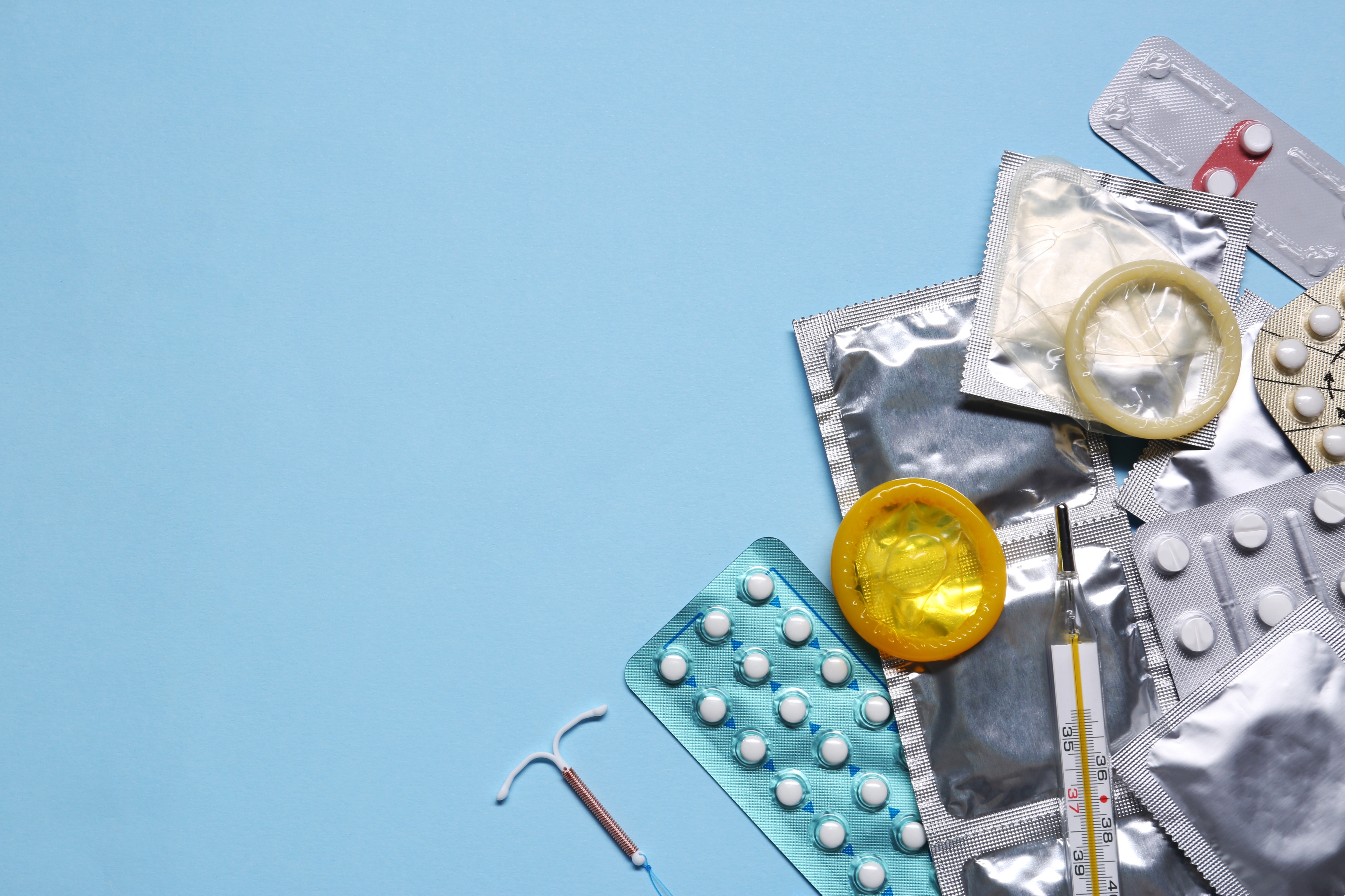 Contraceptive,Pills,,Condoms,,Intrauterine,Device,And,Thermometer,On,Light,Blue